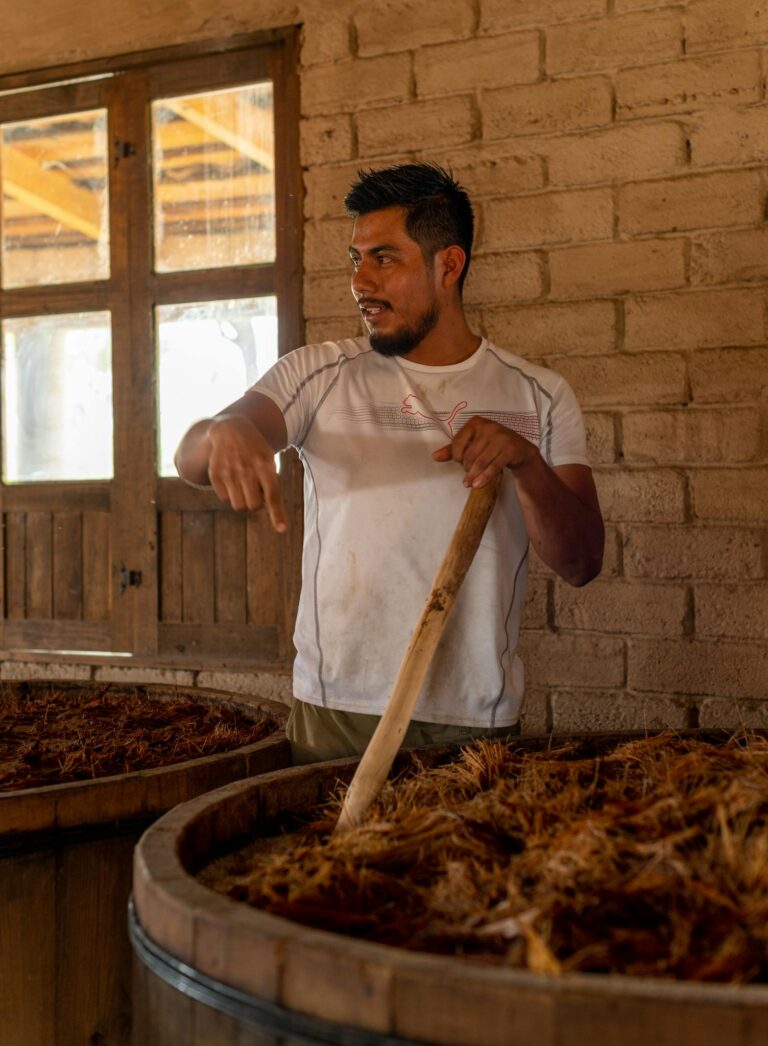 A man stirs agave for tequila fermentation inside a rustic distillery.