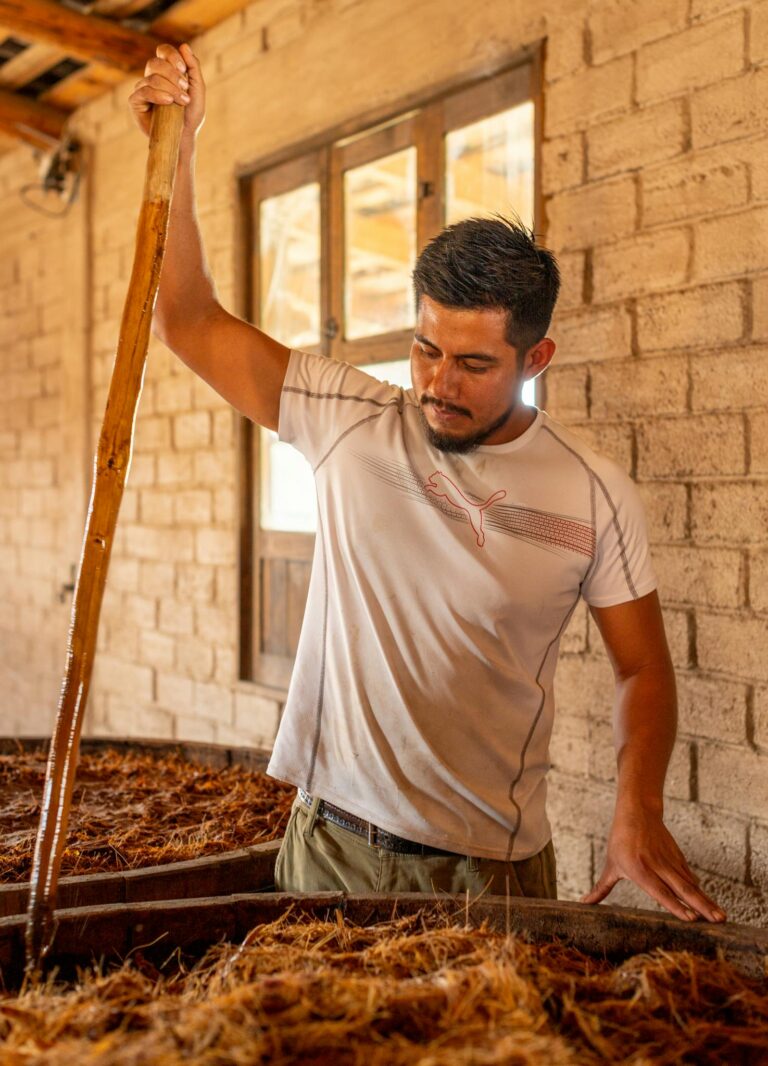 Young man stirring ingredients in tequila production, showcasing tradition and culture.